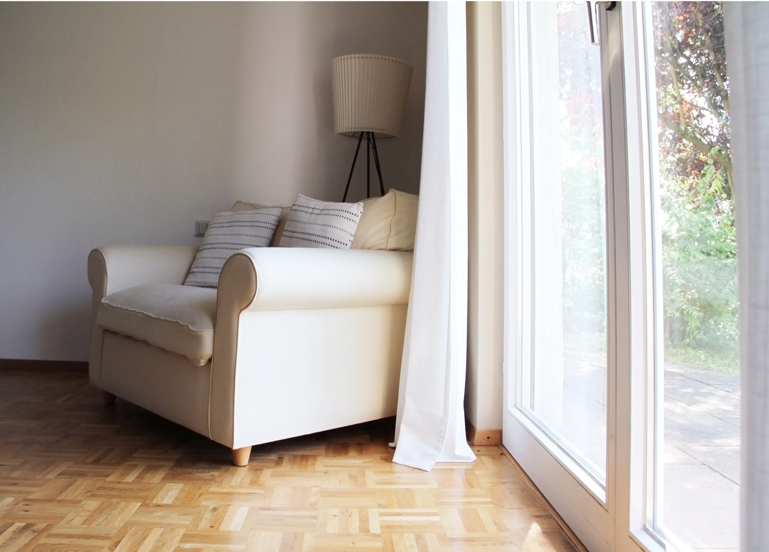 Heller Sessel mit Kissen und Stehleuchte am bodentiefen Fenster des Apartments